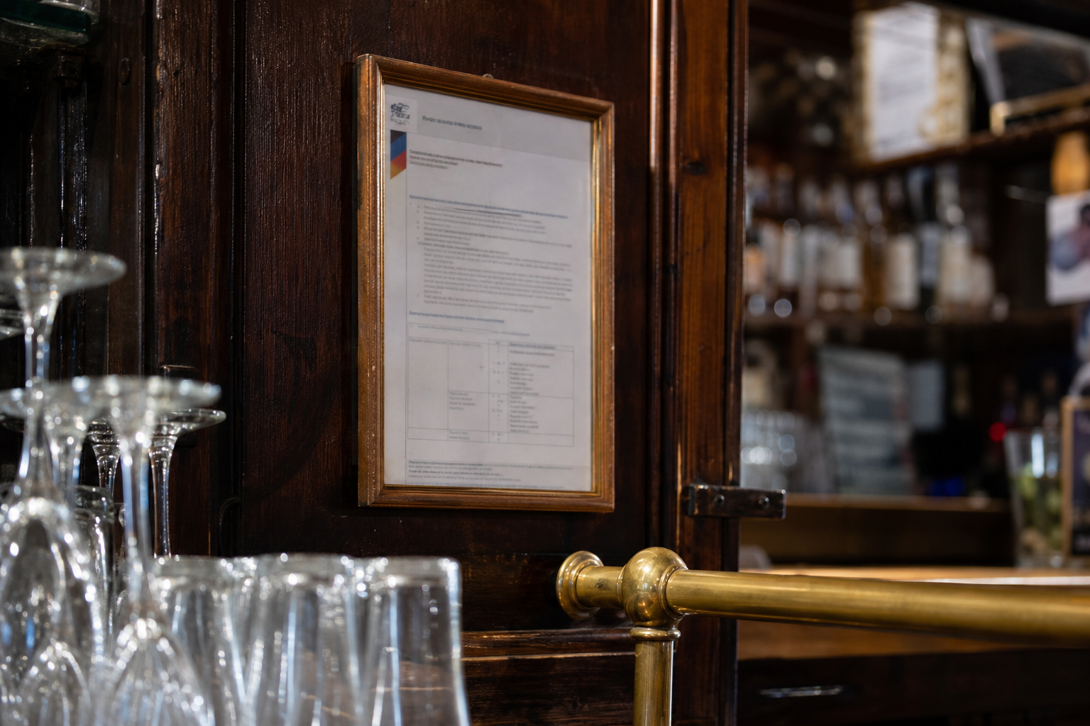 Gros plan sur un document réglementaire encadré derrière un comptoir de bar, avec verres et bouteilles floutés en arrière-plan.